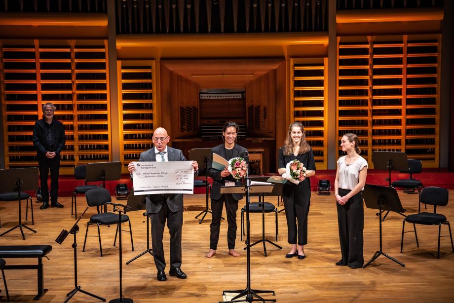 Die Preisträger mit Blumensträußen beim Domnick Cello Wettbewerb 2022. Michael Hörrmann hält einen öbergroßen Scheck mit dem Preisgeld in beiden Händen.