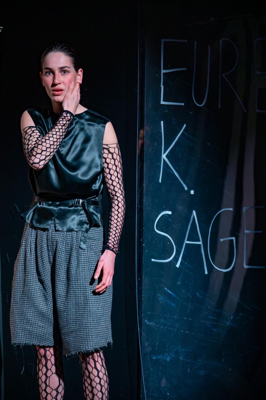 EIne Frau steht neben einer beschrieben Wand und hält sich die Wange