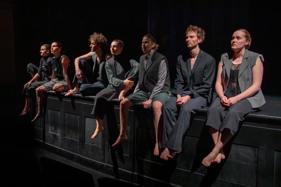 Sieben Menschen sitzen nebeneinander auf der Bühnenkante