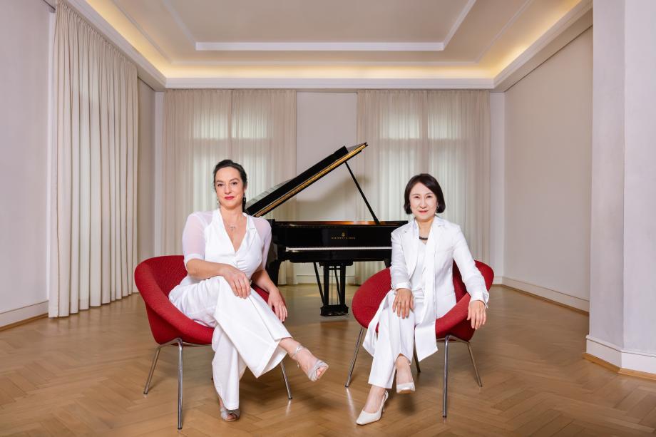 FRanzsika Dannheim und Jeong-Min Kim sitzen - beide ganz in weiß gekleidet - in roten Sesseln vor einem schwarzen Flügel