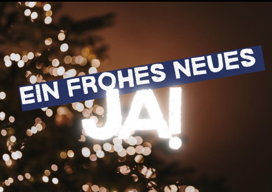 Schriftzug: Ein frohes neues Ja!, im Hintergrund leuchtet ein Weihnachtsbaum