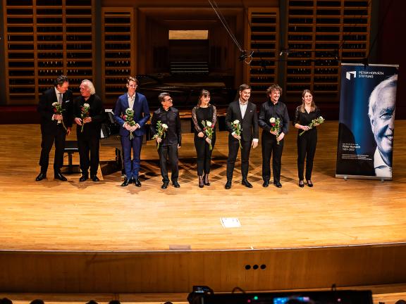 Mehrere festlich gekleidete Personen stehen während dem Abschiedsapplaus auf der Bühne, sie halten Blumen in der Hand.