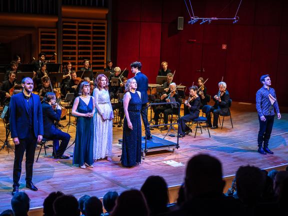 Opernensemble mit Kammerorchester auf dem Podium.