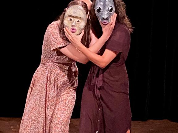 Zwei Frauen halten sich gegenseitig jeweils eine Maske vors Gesicht