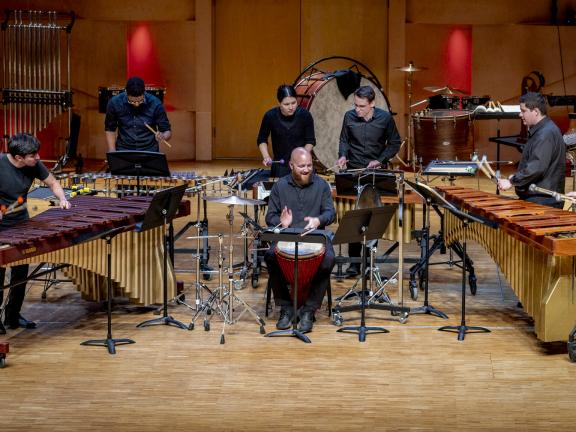Percussionensemble mit verschiedenen Schlagzeuginstrumenten auf einem Konzertpodium.