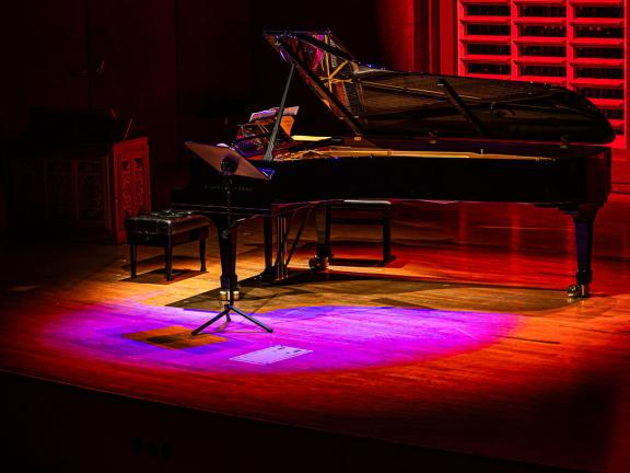 Schwarzer Flügel steht auf Bühne und ist mit rot-pinkem Scheinwerferlicht angestrahlt.