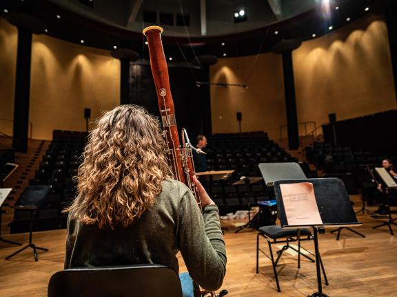 Fagottstudentin sitzt auf der Konzertsaalbühne und schaut in den Zuschauerraum.