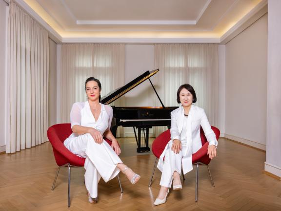 FRanzsika Dannheim und Jeong-Min Kim sitzen - beide ganz in weiß gekleidet - in roten Sesseln vor einem schwarzen Flügel