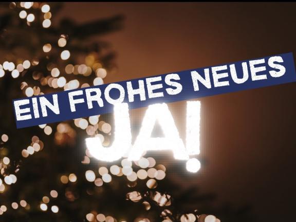 Schriftzug: Ein frohes neues Ja!, im Hintergrund leuchtet ein Weihnachtsbaum