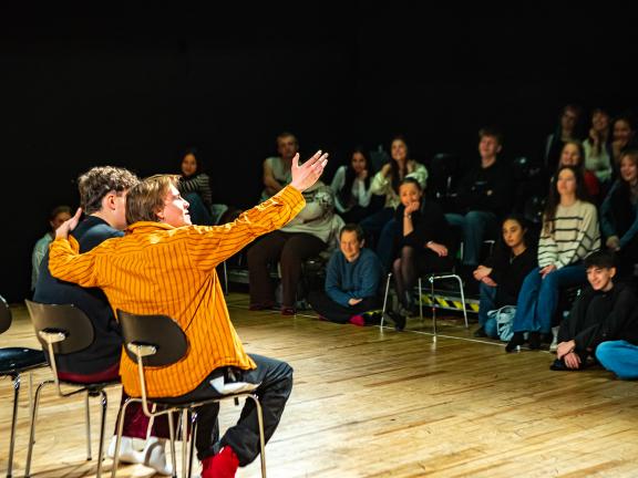 Zwei Schauspielstudierende agieren auf der Arbeitsbühne. Im Publikum sitzen Schülerinnen und Schüler beim Studieninformationstag