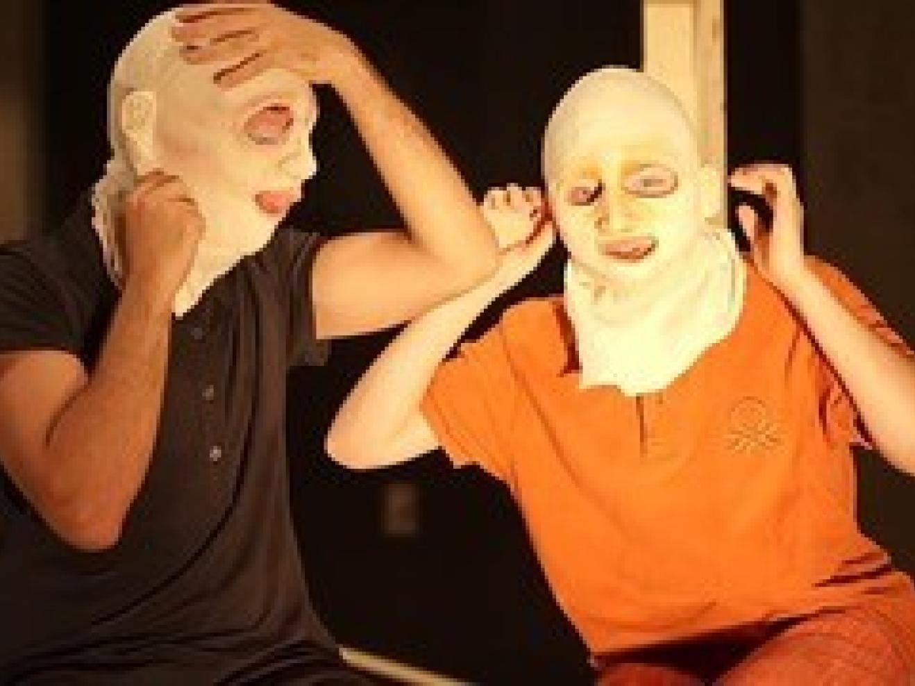 zwei Studierende sitzen nebeneinander mit Masken auf dem Kopf. Sie haben ihre Hände an ihren Masken.